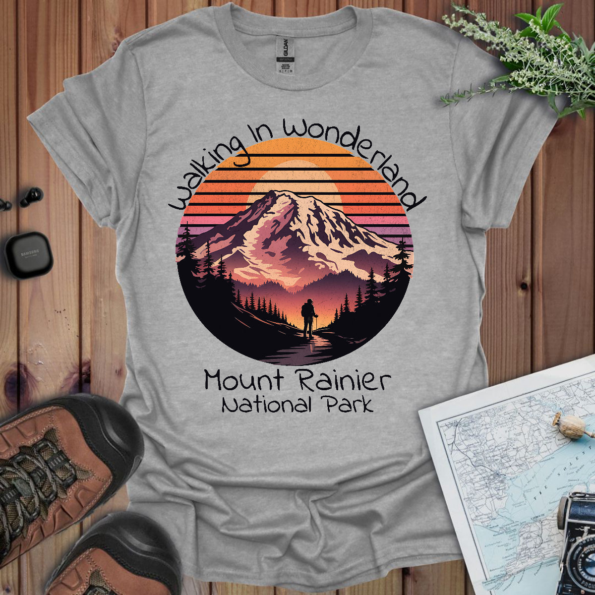 Gray t-shirt with Mount Rainier National Park design on a wooden surface with hiking gear.