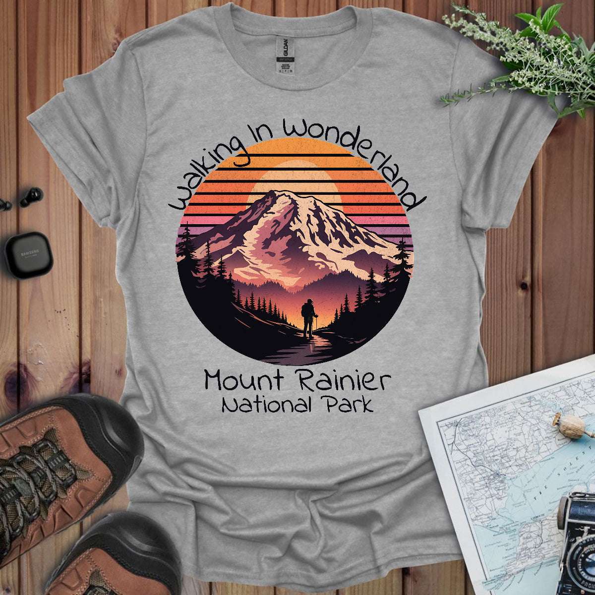 Gray t-shirt with Mount Rainier National Park design on a wooden surface with hiking gear.