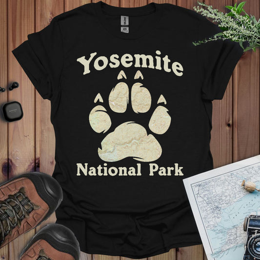 Black t-shirt with Yosemite National Park paw print design on a wooden surface with hiking gear.