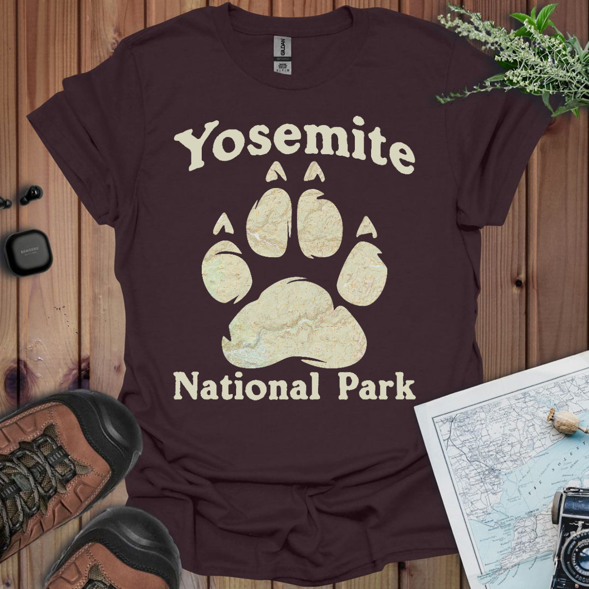 Brown t-shirt with Yosemite National Park paw print design on a wooden surface with hiking gear.