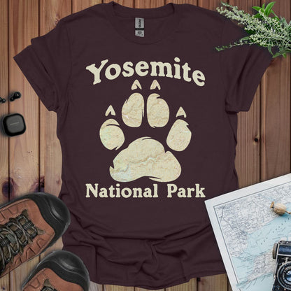 Brown t-shirt with Yosemite National Park paw print design on a wooden surface with hiking gear.