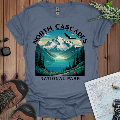 Blue t-shirt with North Cascades National Park graphic on a wooden surface with hiking gear.