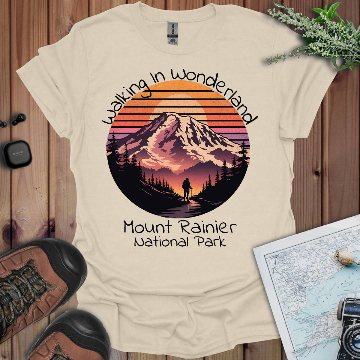 Beige t-shirt with Mount Rainier National Park design on a wooden surface with hiking gear.