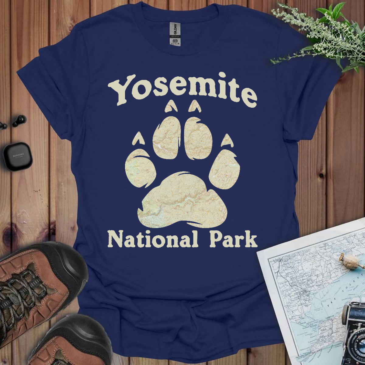 Navy blue t-shirt with Yosemite National Park paw print design on a wooden surface with hiking gear.