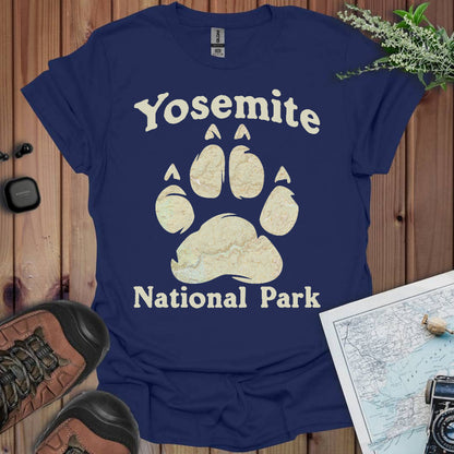 Navy blue t-shirt with Yosemite National Park paw print design on a wooden surface with hiking gear.