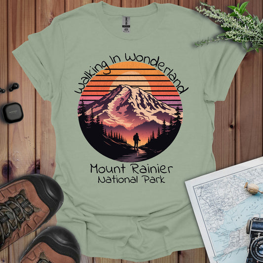 Light green t-shirt with Mount Rainier National Park graphic and text on a wooden surface with hiking gear.