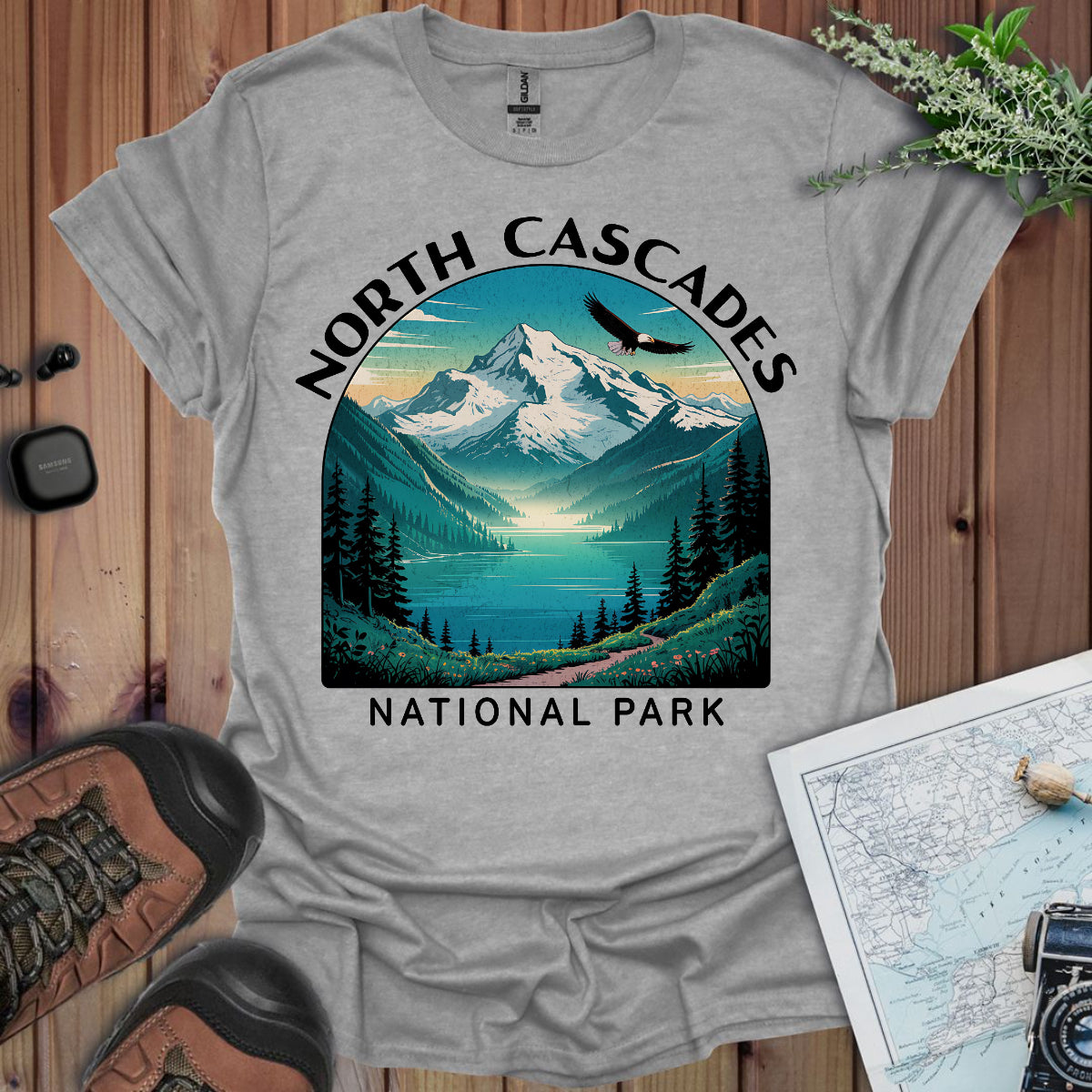 Gray t-shirt with North Cascades National Park design on a wooden surface with hiking gear.