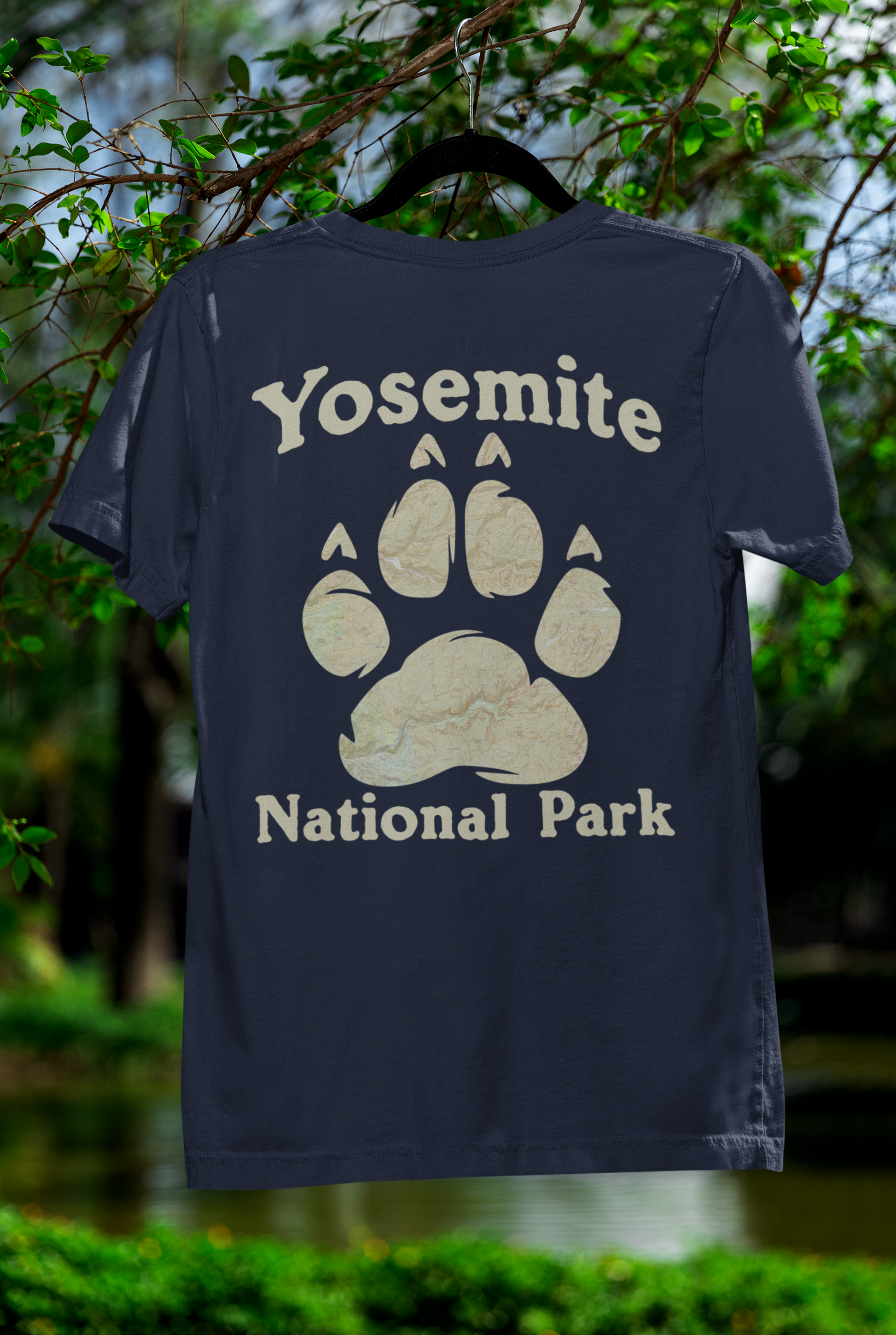Navy blue t-shirt with Yosemite National Park paw print design on a hanger against a natural background.