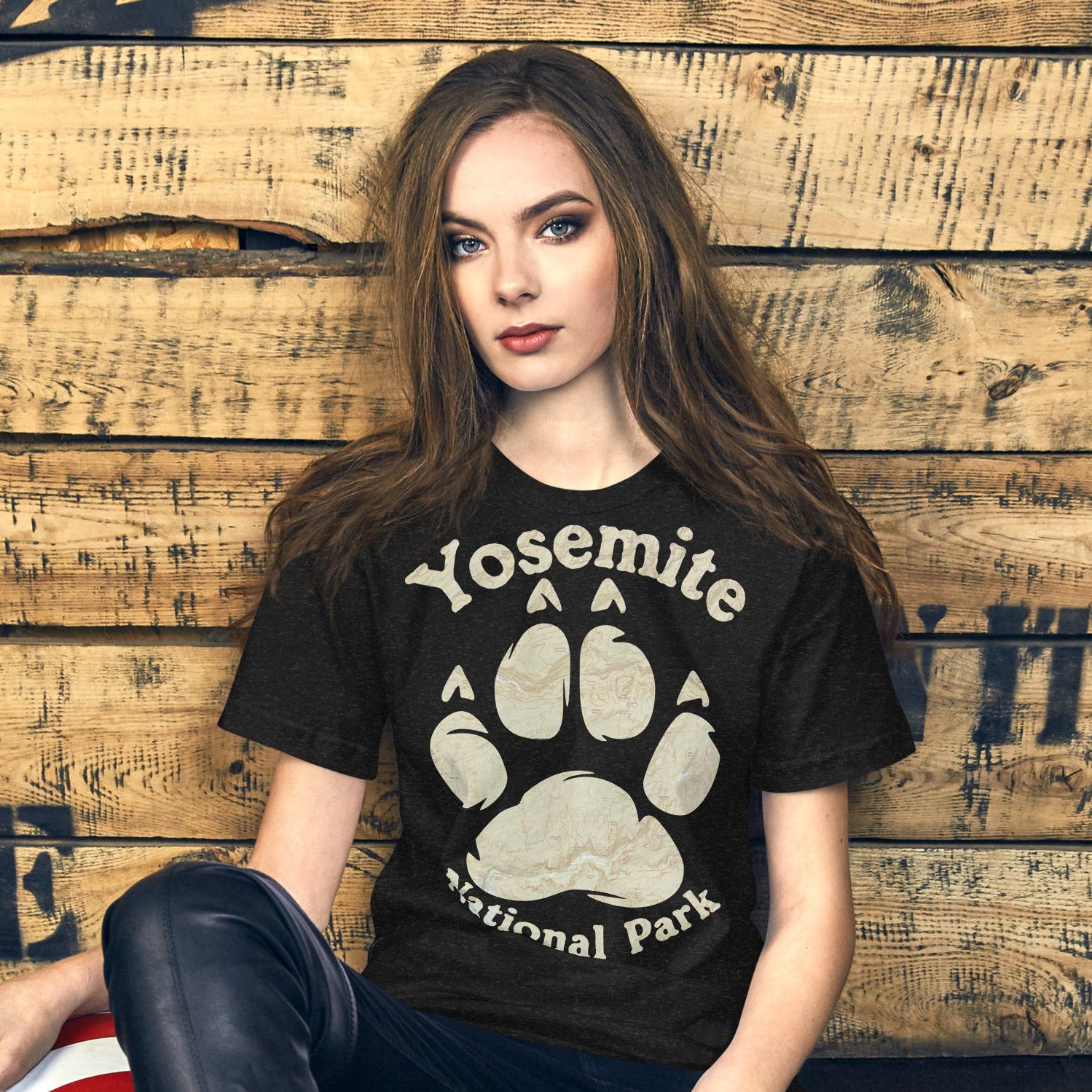 Woman wearing a black t-shirt with Yosemite National Park design, sitting against a wooden wall.